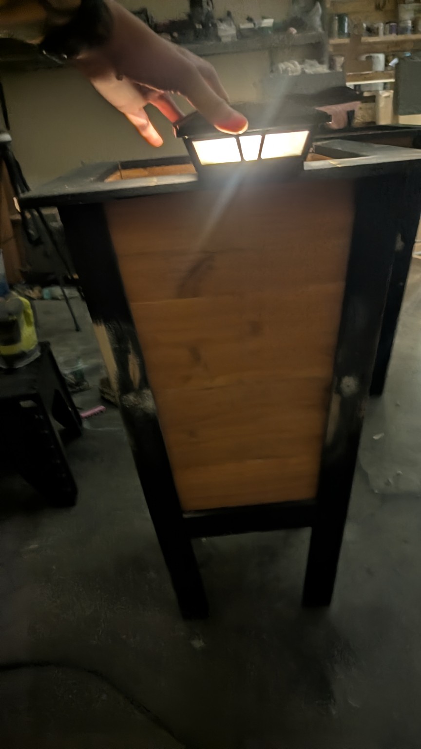 An actual Object and Grove cedar planter in the workshop with black legs and trim; a light is being held above it for a fit check